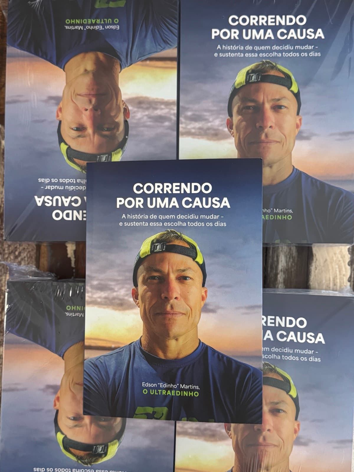 Pilha de exemplares impressos do livro Correndo por uma Causa, ainda embalados, com um exemplar aberto pra frente por cima
